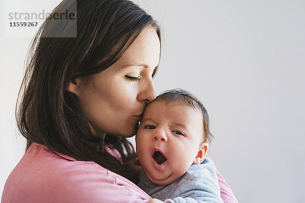 Frau hält und küsst ein Baby gähnend