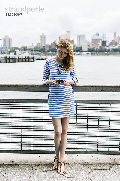 USA  New York City  Junge Frau steht in Manhattan mit Smartphone
