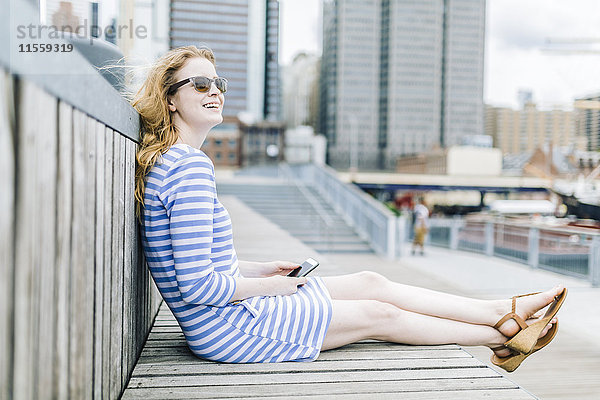 Junge Frau am Pier sitzend mit dem Handy