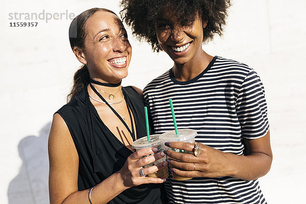 Zwei lachende Frauen stoßen mit Getränken in Plastikbechern an.