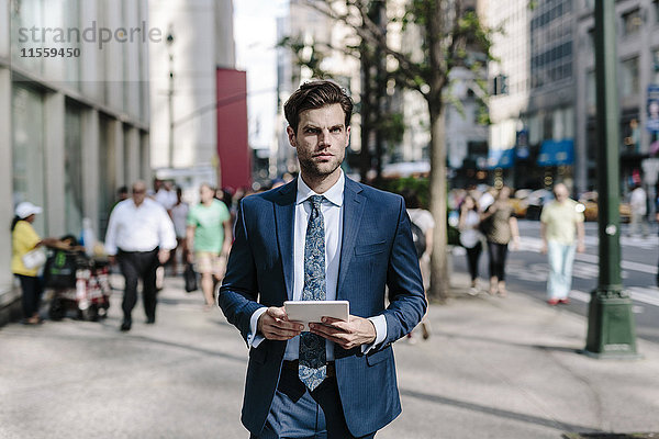Ein hübscher Geschäftsmann  der in Manhattan spazieren geht und ein digitales Tablett bei sich trägt.