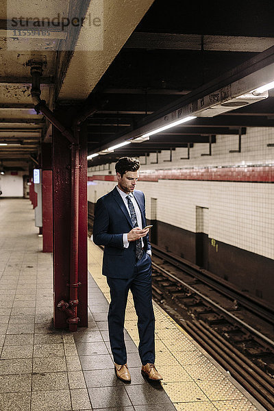 Geschäftsmann steht an einer New Yorker U-Bahn-Station mit Smartphone
