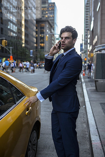 Geschäftsmann am Telefon  der in ein Taxi in Manhattan einsteigt.