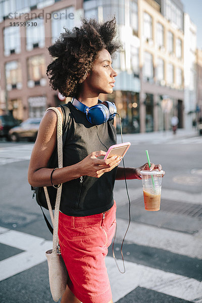 Junge Frau mit Kopfhörer und Smartphone Crossong Street in Brooklyn  carying take away drink