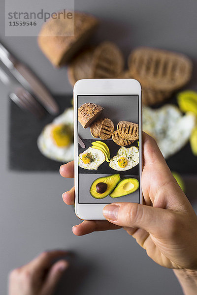 Handaufnahme eines Smartphone Fotos vom Frühstück mit Avocados und Eiern