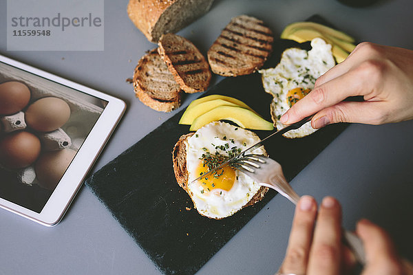 Frühstück mit Eiern  Avovados und geröstetem Brot auf einem Tisch mit digitaler Tablette