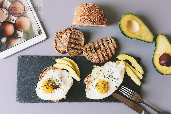 Frühstück mit Eiern  Avovados und geröstetem Brot auf einem Tisch mit digitaler Tablette