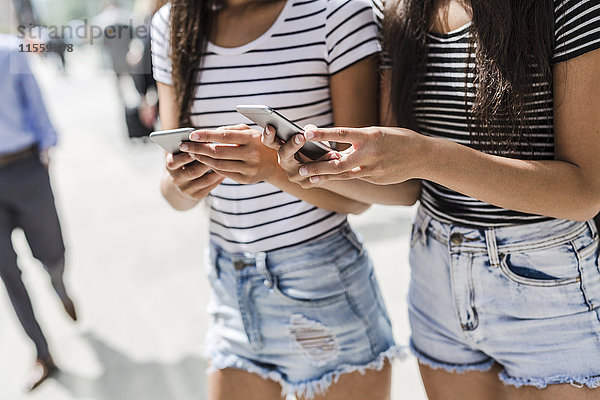 Zwei junge Frauen halten Handys in der Stadt.
