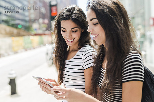 USA  New York City  zwei glückliche Zwillingsschwestern beim Blick auf Handys in Manhattan