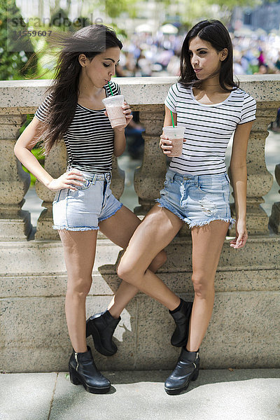 Zwei Zwillingsschwestern im Freien bei einem Getränk zum Mitnehmen
