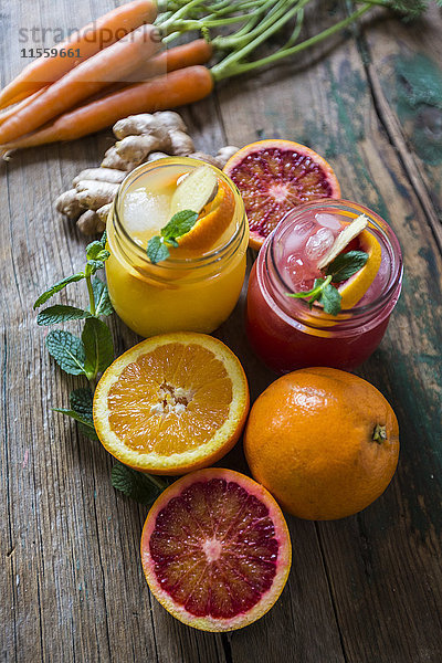 Zwei Gläser mit verschiedenen Orangensäften  Orangen  Karotten  Minzeblättern und Ingwer.