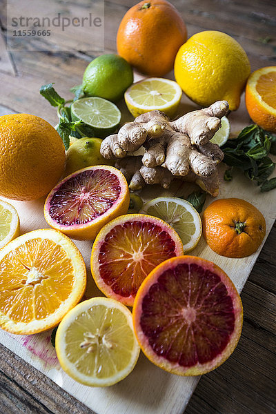 Geschnittene und ganze Zitronen  Orangen und Limetten  Ingwerwurzel und Minzblätter auf Holzbrettchen