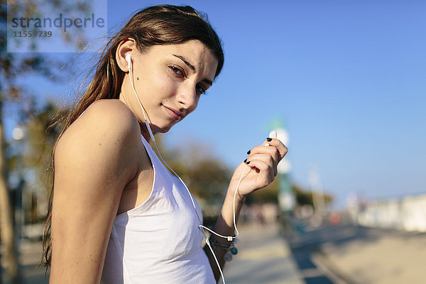 Junge Frau entspannt sich bei Sonnenuntergang an der Strandpromenade und hört Musik mit Kopfhörern.