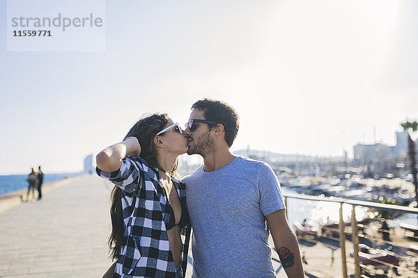 Ein glückliches junges Paar  das am Hafen spazieren geht und sich küsst.
