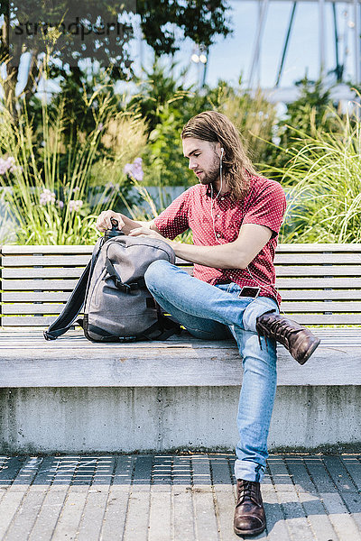 Mann sitzt auf einer Bank mit Ohrstöpseln und Rucksack