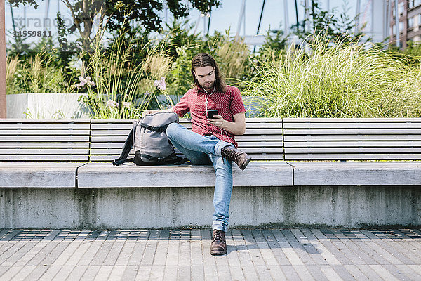 Mann sitzt auf einer Bank mit Ohrstöpseln mit Handy