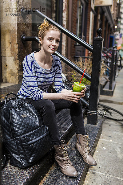 USA  New York City  Frau  die in Manhattan auf der Treppe sitzt und einen Smoothie trinkt.