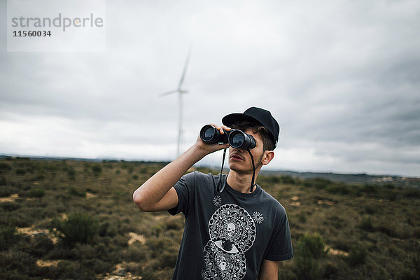 Spanien  Lleida  junger Mann schaut durchs Fernglas in ländlicher Landschaft