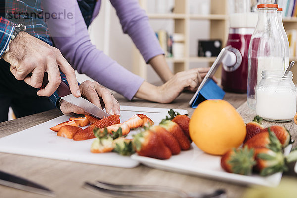 Mann hackt Erdbeeren während seine Freundin mit Tablette  Teilansicht