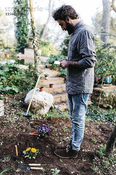 Mann fotografiert mit einer im Garten gepflanzten Blumentablette