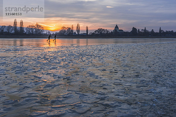 Deutschland  zwei Eisläufer auf dem zugefrorenen Bodensee mit der Insel Reichenau im Hintergrund bei Sonnenuntergang