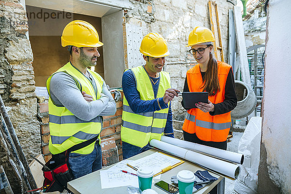 Frau und zwei Bauarbeiter mit Tablette auf der Baustelle