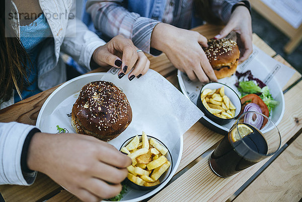 Frauenhände essen Hamburger und Pommes frites