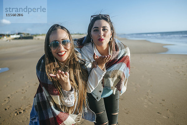 Porträt von zwei jungen Frauen am Strand  die Küsse blasen