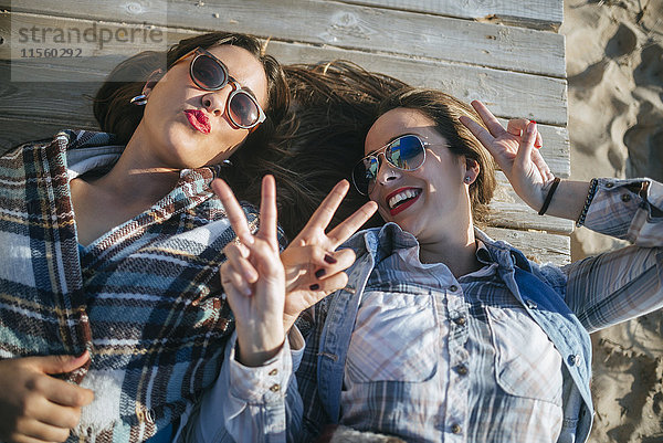 Zwei junge Frauen auf Holzsteg liegend mit Siegeszeichen