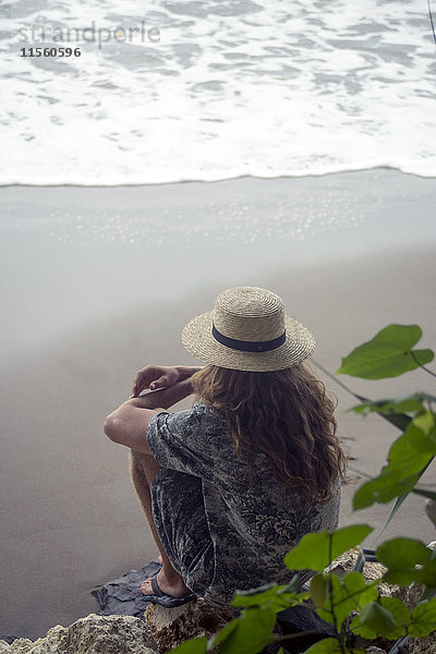 Indonesien  Java  Frau mit Strohhut auf Felsen am Strand mit Blick aufs Meer