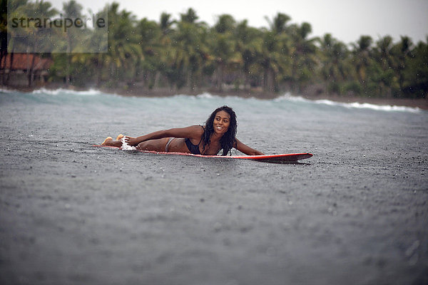 Indonesien  Java  Frau auf dem Surfbrett auf dem Meer im Regen liegend