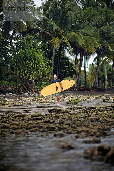 Indonesien  Java  Mann mit Surfbrett an der Küste