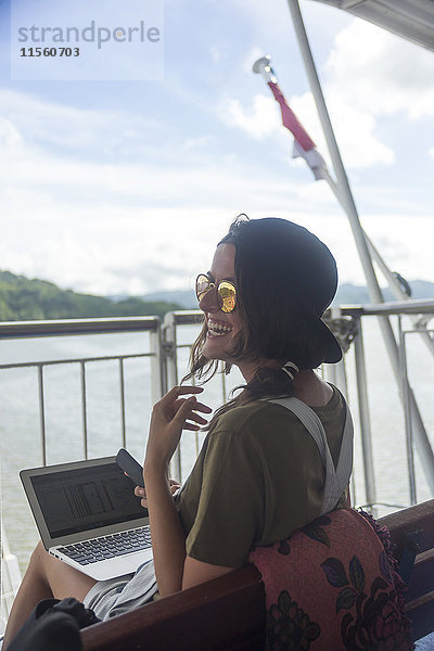 Indonesien  Insel Lombok  glückliche Frau mit Laptop auf dem Schiffsdeck