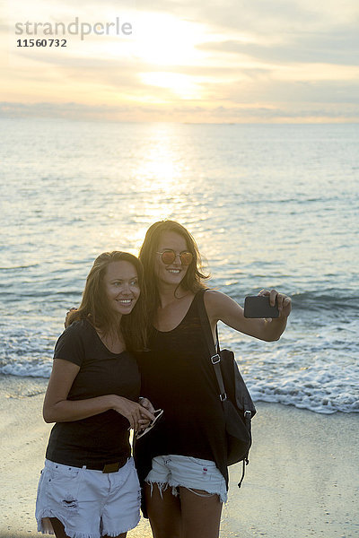 Indonesien  Bali  zwei Frauen mit einem Selfie am Strand bei Sonnenuntergang