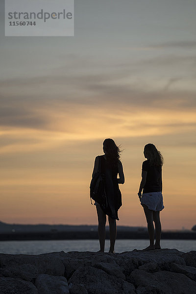 Indonesien  Bali  zwei Frauen beobachten den Sonnenuntergang über dem Meer