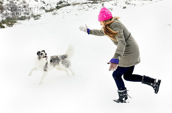 Junge Frau spielt mit ihrem Hund im Schnee