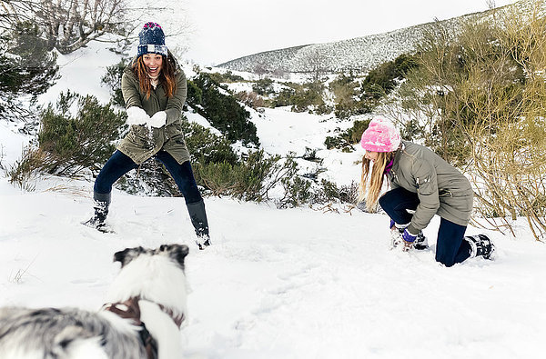 Zwei Freunde spielen mit ihrem Hund im Schnee.