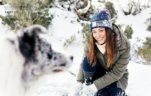 Schöne Frau  die mit ihrem Hund im Schnee spielt.