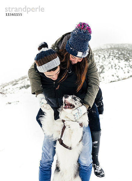 Junges Paar spielt mit seinem Hund im Schnee