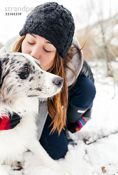Junge Frau küsst ihren Hund im Schnee