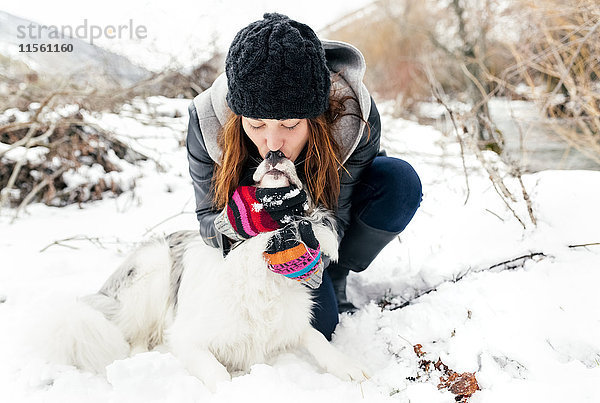 Junge Frau küsst ihren Hund im Schnee