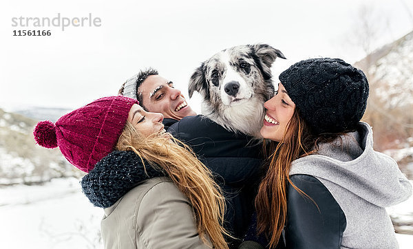 Drei Freunde haben Spaß mit einem Hund im Schnee