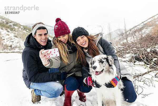 Drei Freunde  die Spaß daran haben  einen Selfie mit einem Hund im Schnee zu nehmen.