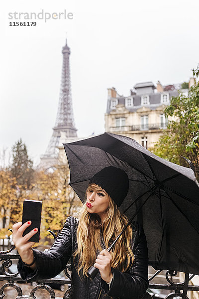 Frankreich  Paris  junge Frau  die einen Selfie mit dem Eiffelturm im Hintergrund nimmt.