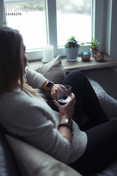 Junge Frau mit einem Glas Kaffee auf der Couch zu Hause beim Blick auf smartwatch