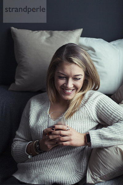 Lächelnde  blonde Frau mit einem Glas Kaffee auf der Couch zu Hause.