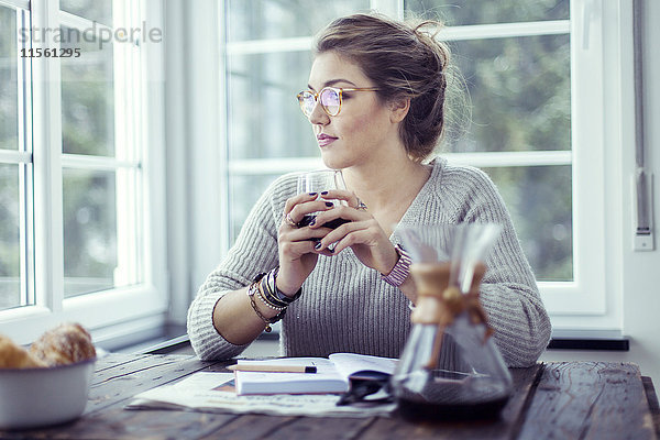 Junge Frau beim Kaffeetrinken am Tisch mit Blick durchs Fenster