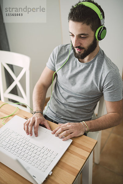 Junger Mann mit Kopfhörer und Laptop