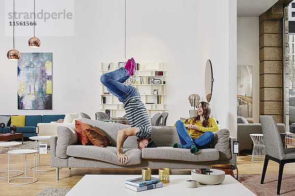 Paar im modernen Möbelhaus mit Kopfstand auf der Couch