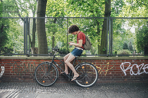 Junger Mann mit Handy auf dem Fahrrad sitzend